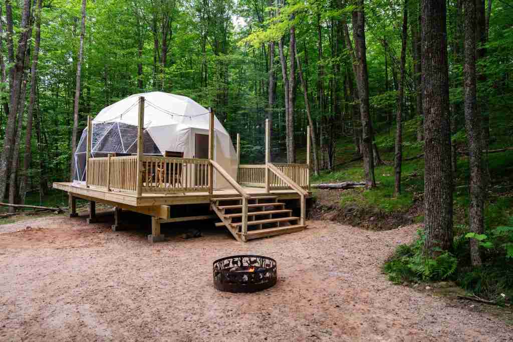 Geodesic glamping dome on a wooden deck surrounded by trees