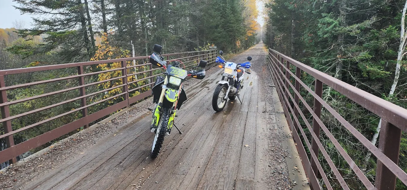 Two dual-sport motorcycles on a trail bridge in the Northwoods